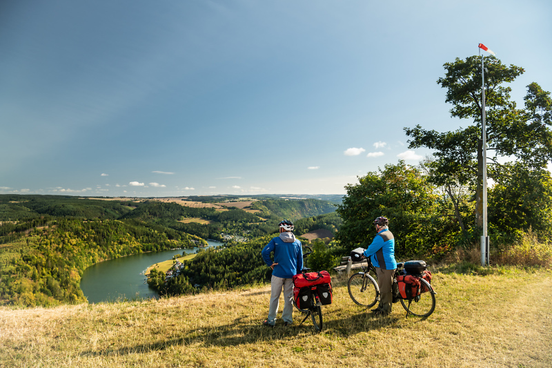 Zwei Radfahrer pausieren und blicken von oben auf eine Saaleschleife am Th&uuml;ringer Meer.