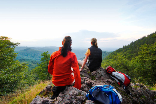 Zwei Frauen sitzen auf einem Felsen und blicken in die Ferne. Sie tragen Wanderkleidung.