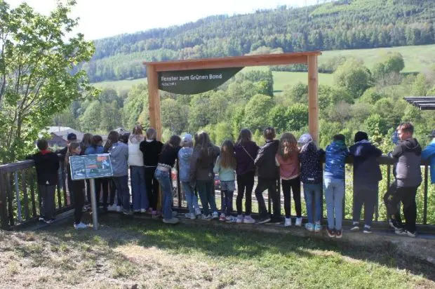Viele Kinder, die durch ein symbolisches "Fenster zum Grünen Band" in eine wunderschöne grüne Landschaft schauen.