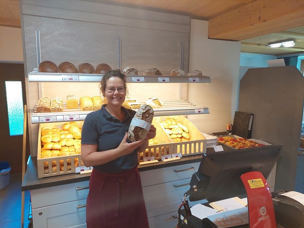 B&auml;ckerei-Verk&auml;uferin h&auml;lt ein Brot mit Banderole in die Kamera. Auf der Banderole steht "Naturpark-Brot".