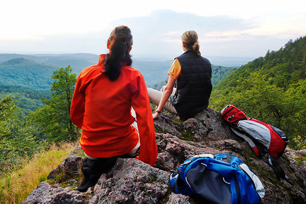 Zwei Frauen sitzen auf einem Felsen und blicken in die Ferne. Sie tragen Wanderkleidung.